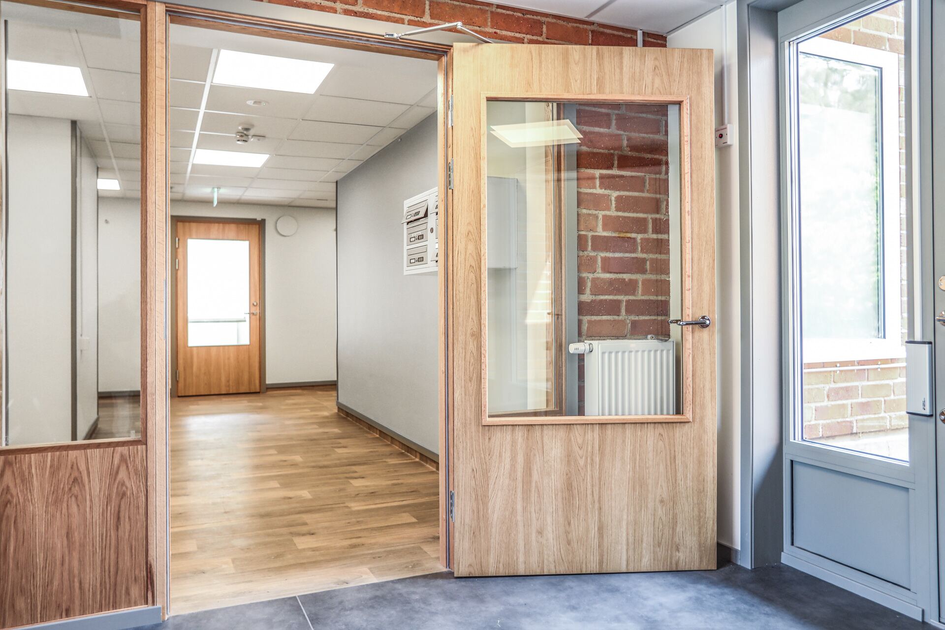 Entré med trädörr, tegelvägg och anslutande korridor på Dalviksgatan 71E.