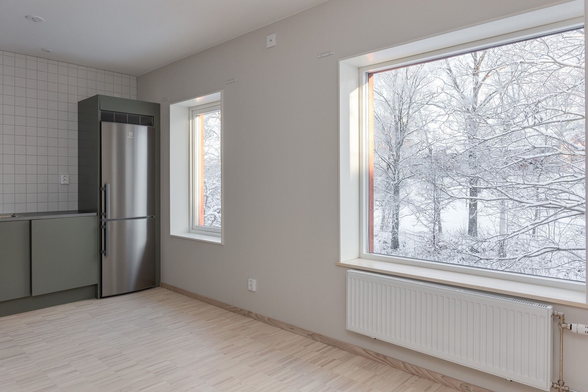 Ljust rum med köksdel och stort fönster mot snötäckta träd på Ryttartorpet 1 i Växjö.